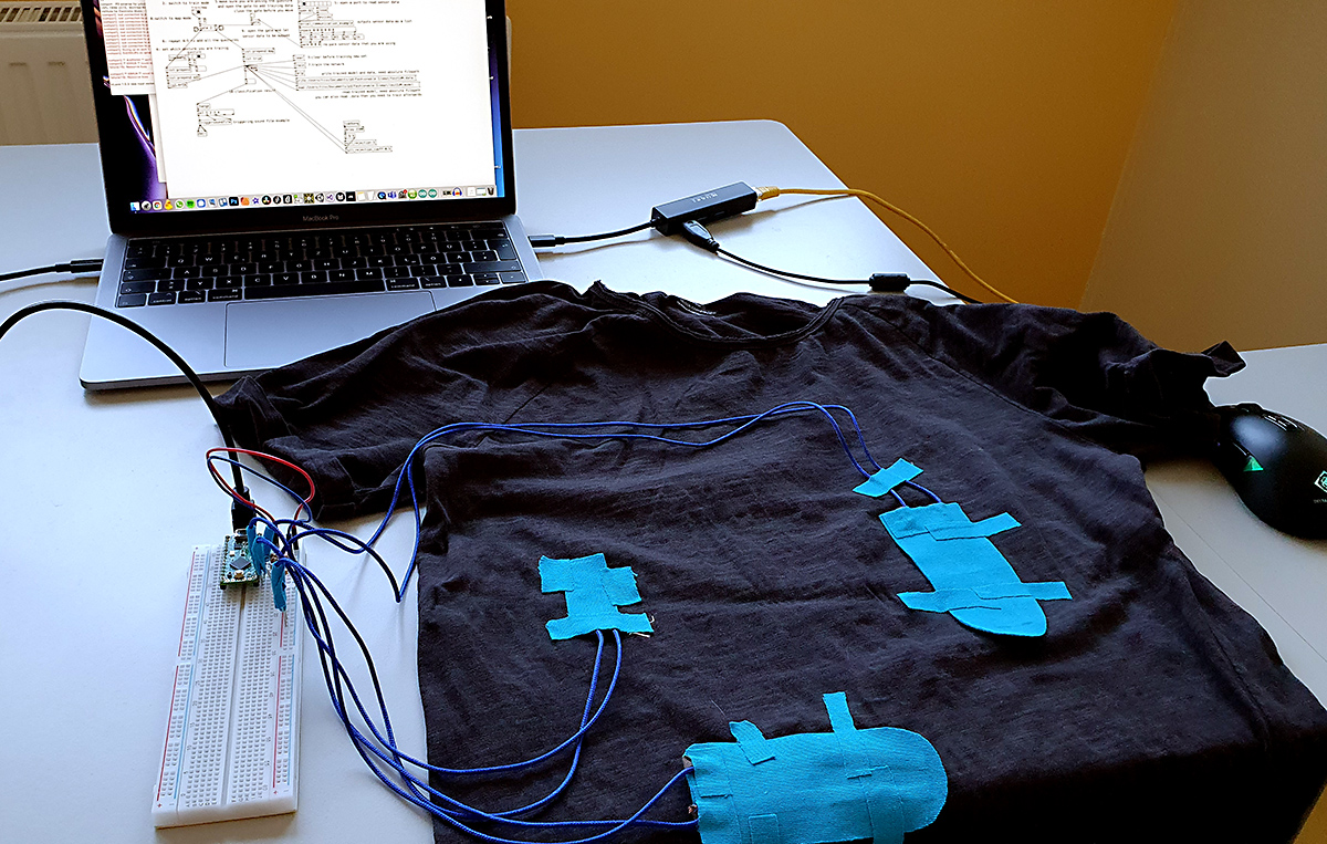A t-shirt with blue tapes, cables are connected to the tape and microcontroller.